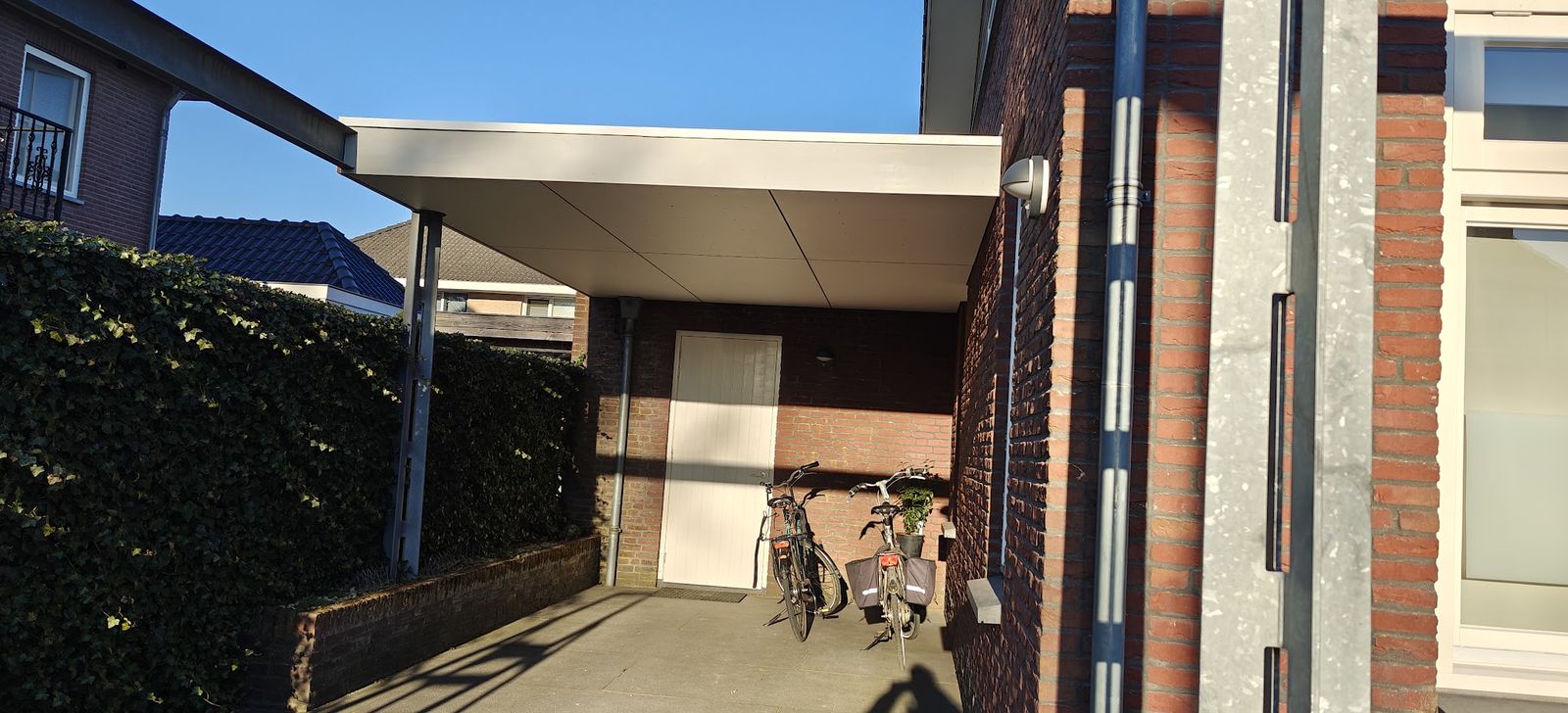 Carport tussen huis en haag met fietsen eronder
